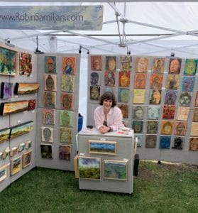 A woman sitting at the table in front of an art display.