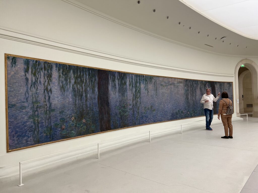 A woman holding a ribbon in front of many paintings.