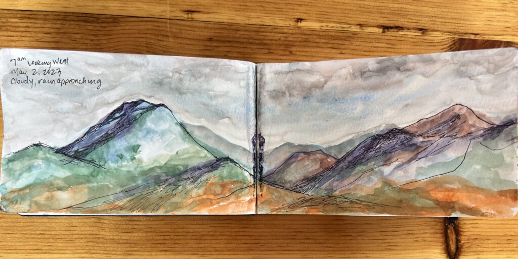 Watercolor mountain landscape in sketchbook on table.