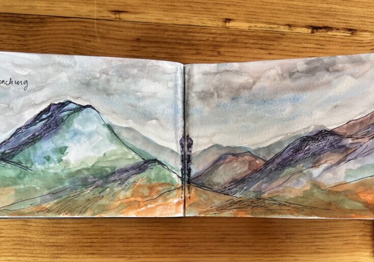 Watercolor mountain landscape in sketchbook on table.