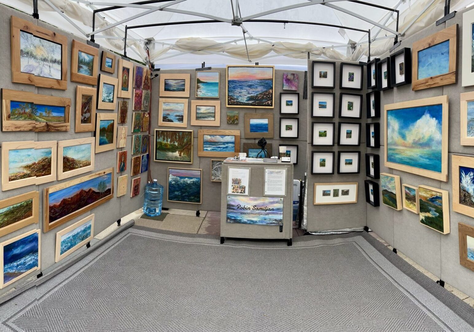 Art tent displaying framed seascape and landscape paintings
